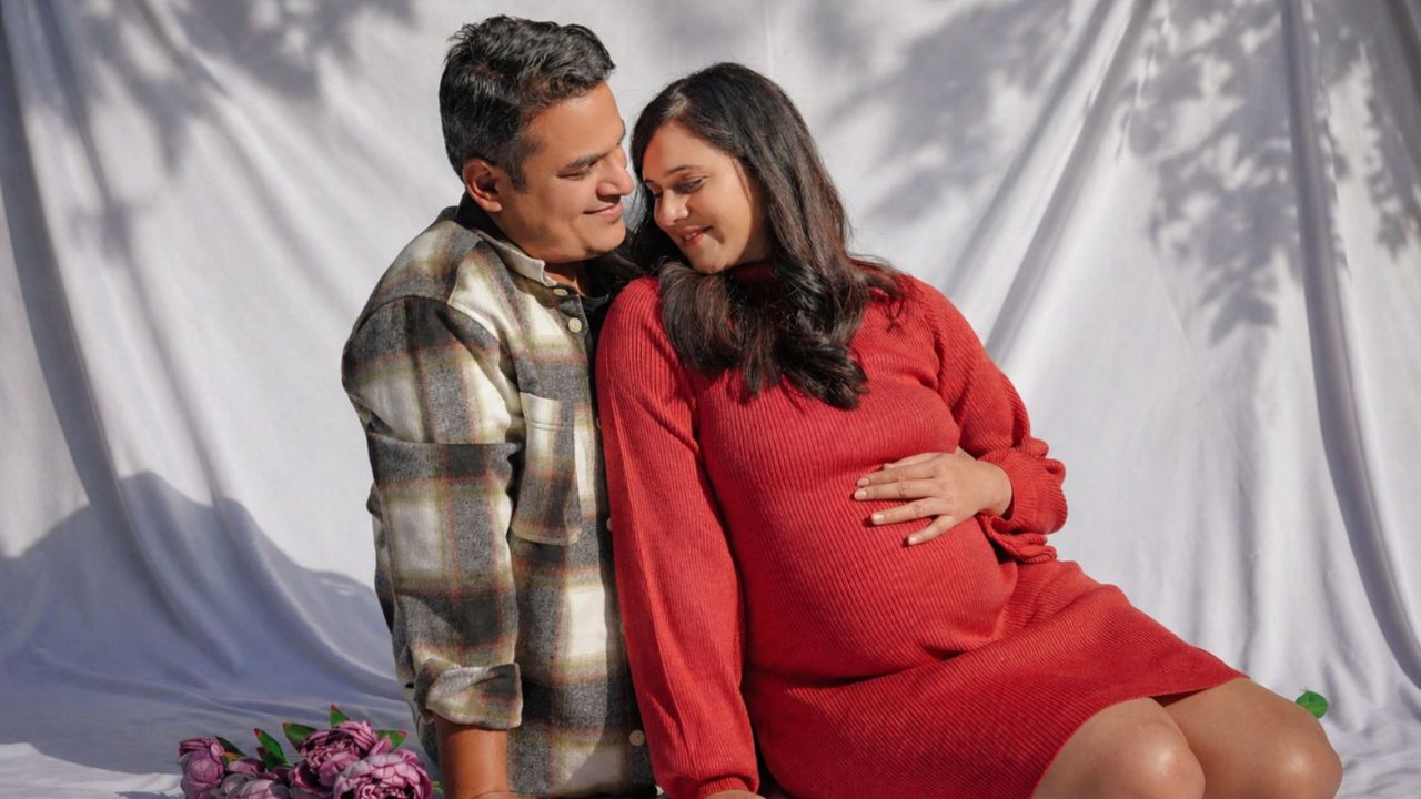 Elegant maternity shoot dress ideas from Indo Frames featuring a flowing red gown for a luxury indoor shoot.