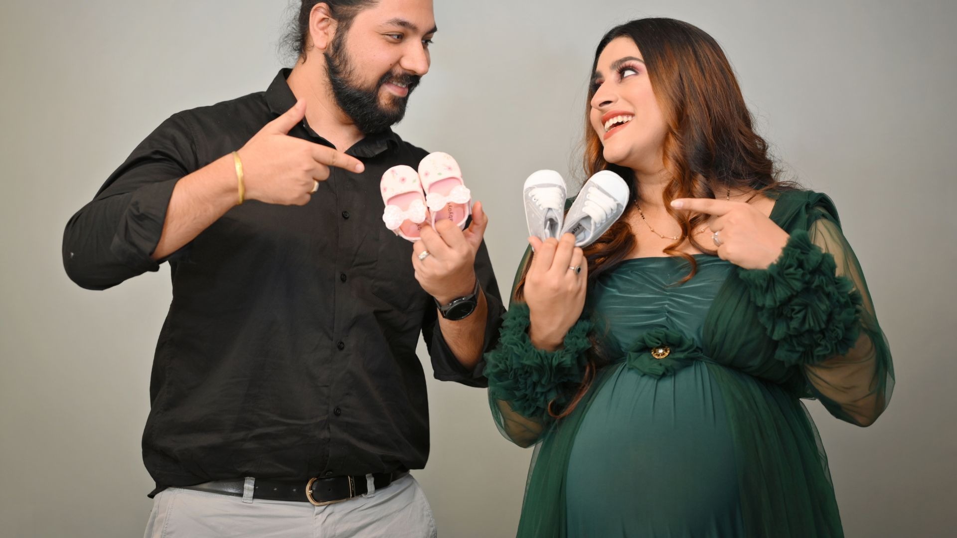 Smiling couple holding pink and blue baby shoes for gender reveal maternity photoshoot by Indo Frames — perfect Instagram caption moment