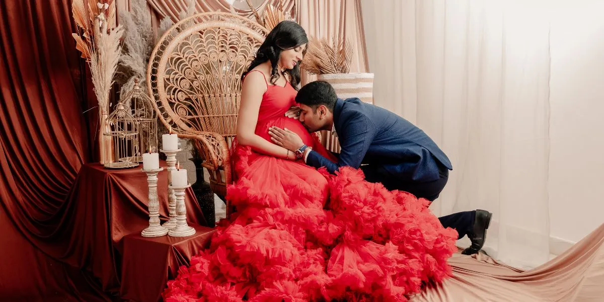 A pregnant woman in a red ruffle dress and her husband posing for a maternity shoot at Indo Frames studio.
